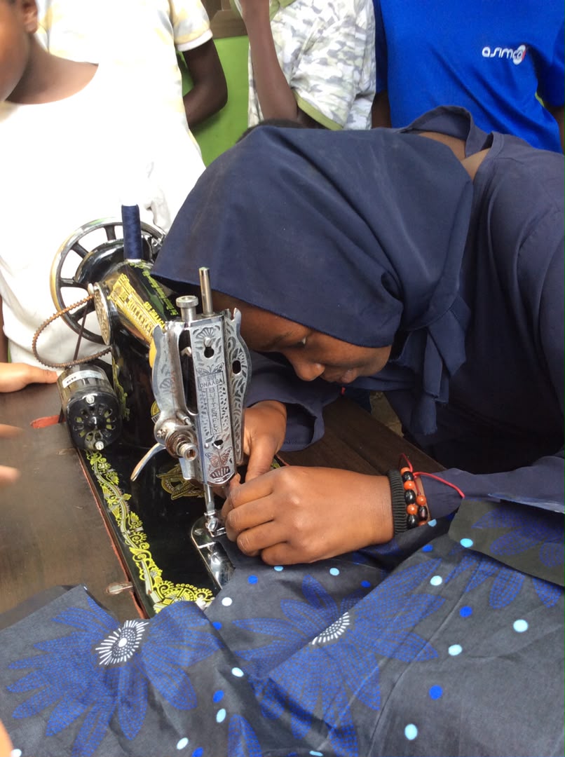 A young Tanzanian woman training on a sewing machine with batik fabric