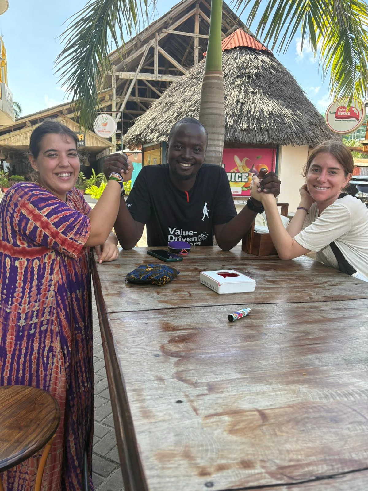 A Tanzanian host and two guests enjoying a warm welcome at a tropical restaurant
