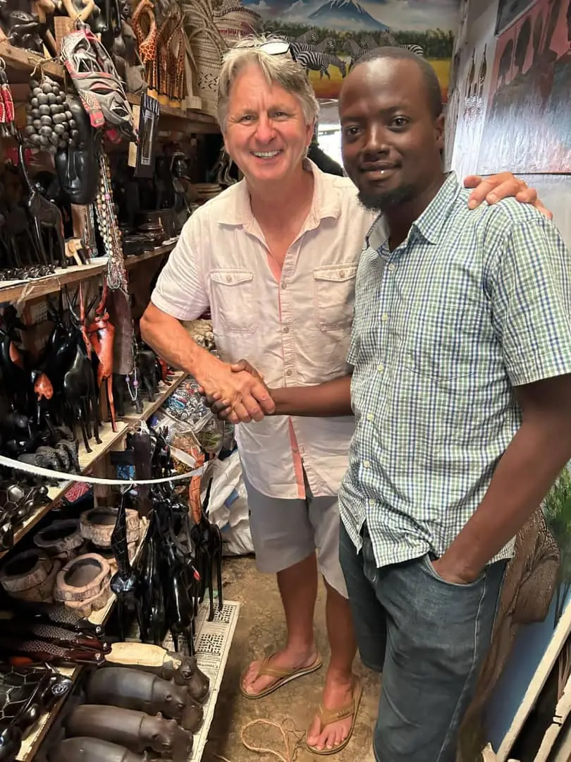 A visitor shaking hands with a craftsman inside a Tanzanian curio market